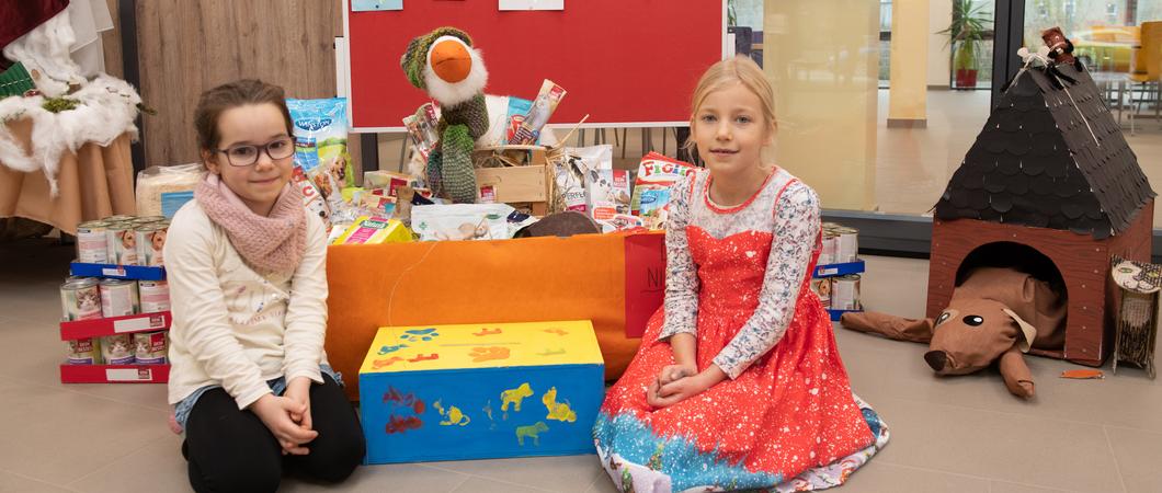 Emilie und Kim präsentieren stolz den bereits gut gefüllten Gabenkorb für Tierfutter und -zubehör sowie die neu gestaltete Box für Geldspenden