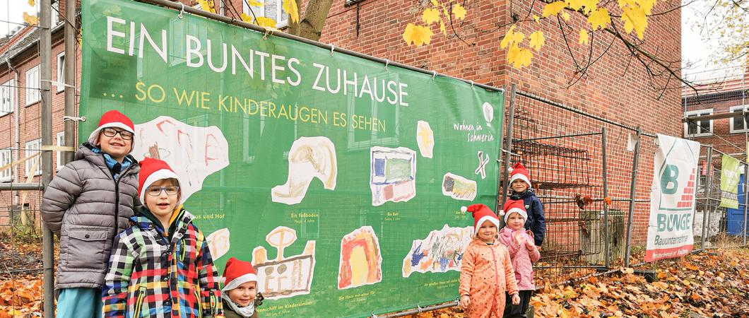 Die Kinder Andrijus, Caspar und Evelyn sowie Emily-Sophie, Linea und Oskar aus der Handwerks-Kita „Alles im Lot“ präsentieren stolz ihre Bauzaunplane