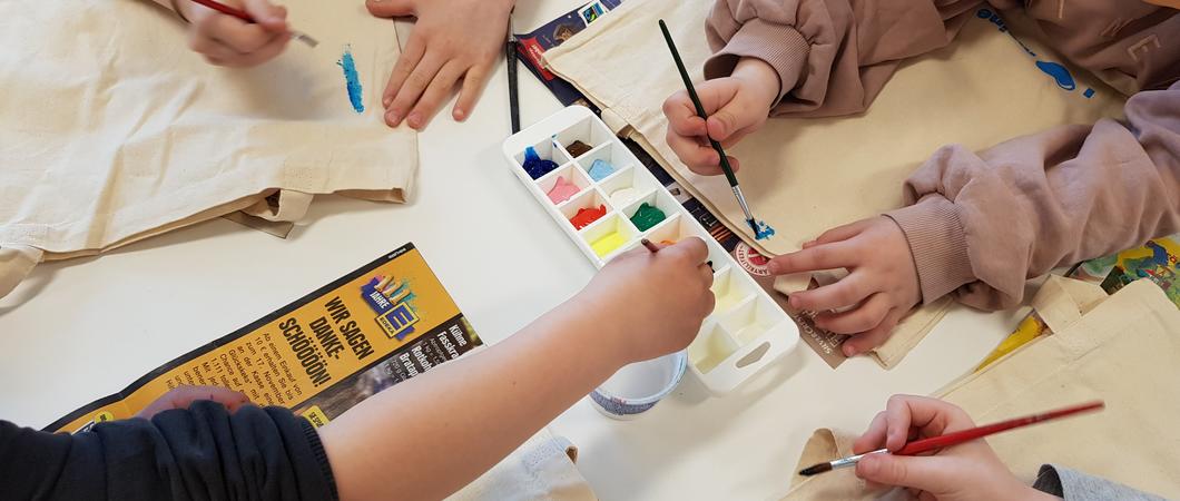 Auf den Tischen legen die Kinder altes Zeitungspapier aus. Sie möchten gleich malen und da soll nichts daneben kleckern. Alle bekommen auch noch Pinsel, Farben und Wasser. Nun schnappt sich jeder einen Stoffbeutel und schon geht es los.