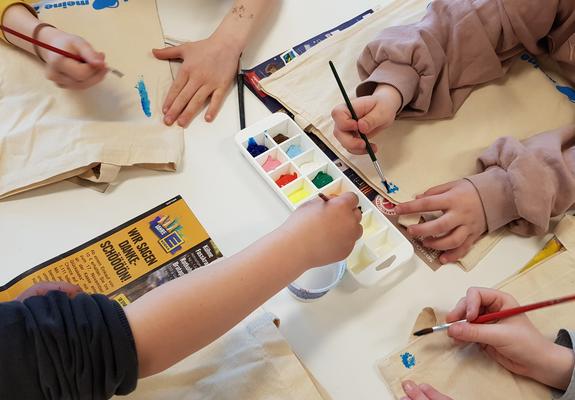 Auf den Tischen legen die Kinder altes Zeitungspapier aus. Sie möchten gleich malen und da soll nichts daneben kleckern. Alle bekommen auch noch Pinsel, Farben und Wasser. Nun schnappt sich jeder einen Stoffbeutel und schon geht es los.