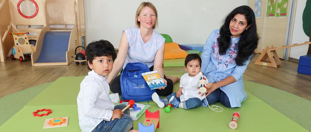 AWO-Mitarbeiterin Katharina Koslow (Mitte) zeigt Mahbuba Afroja (r.) den Willkommensrucksack der Stadt mit dem Familien ABC und vielen nützlichen Dingen, Foto: maxpress